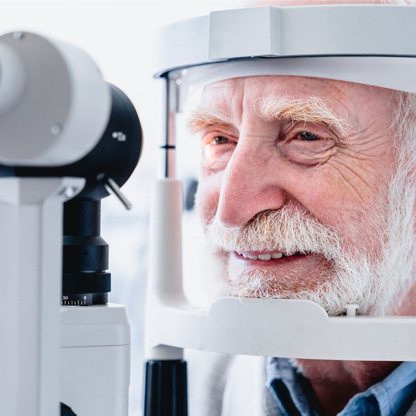Ein älterer Mann mit weißen Bart wird von einem Gerät beim Augenarzt untersucht